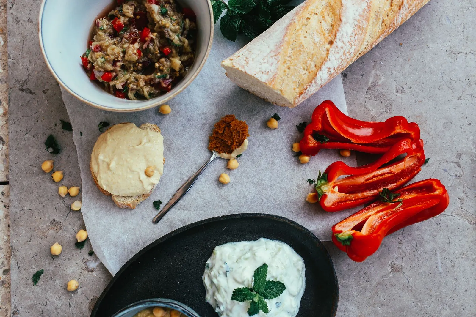 Top view of a Mediterranean spread featuring fresh baguette, dips, and vibrant vegetables.